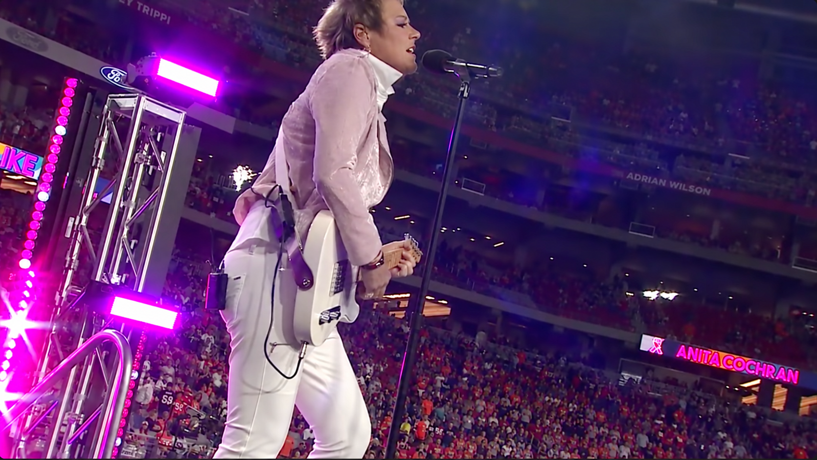 Anita Cochran performing live on a stadium stage with her white electric guitar